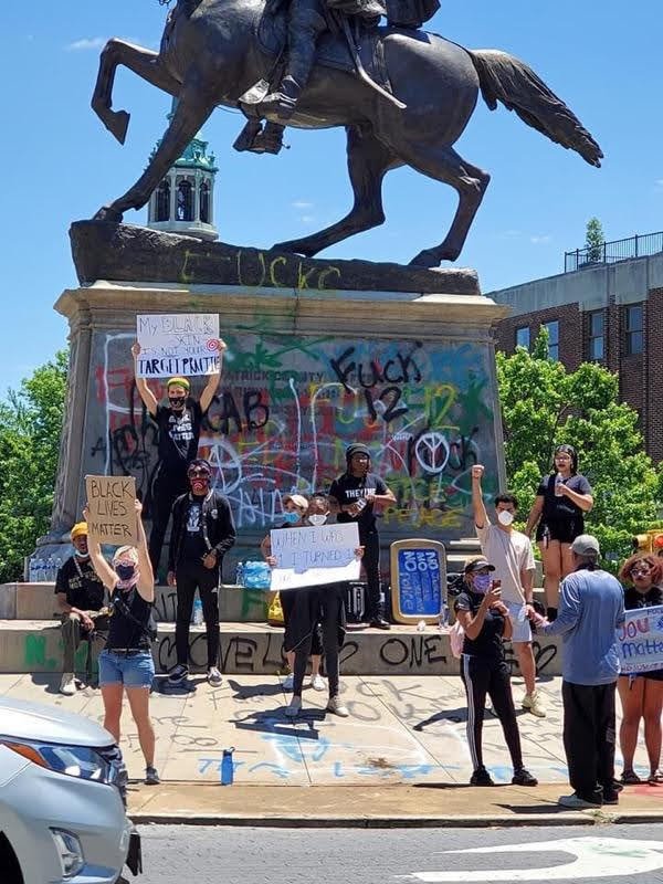 Protester during a George Floyd rally stand in front of a Confederate monument that has been hit with graffiti.